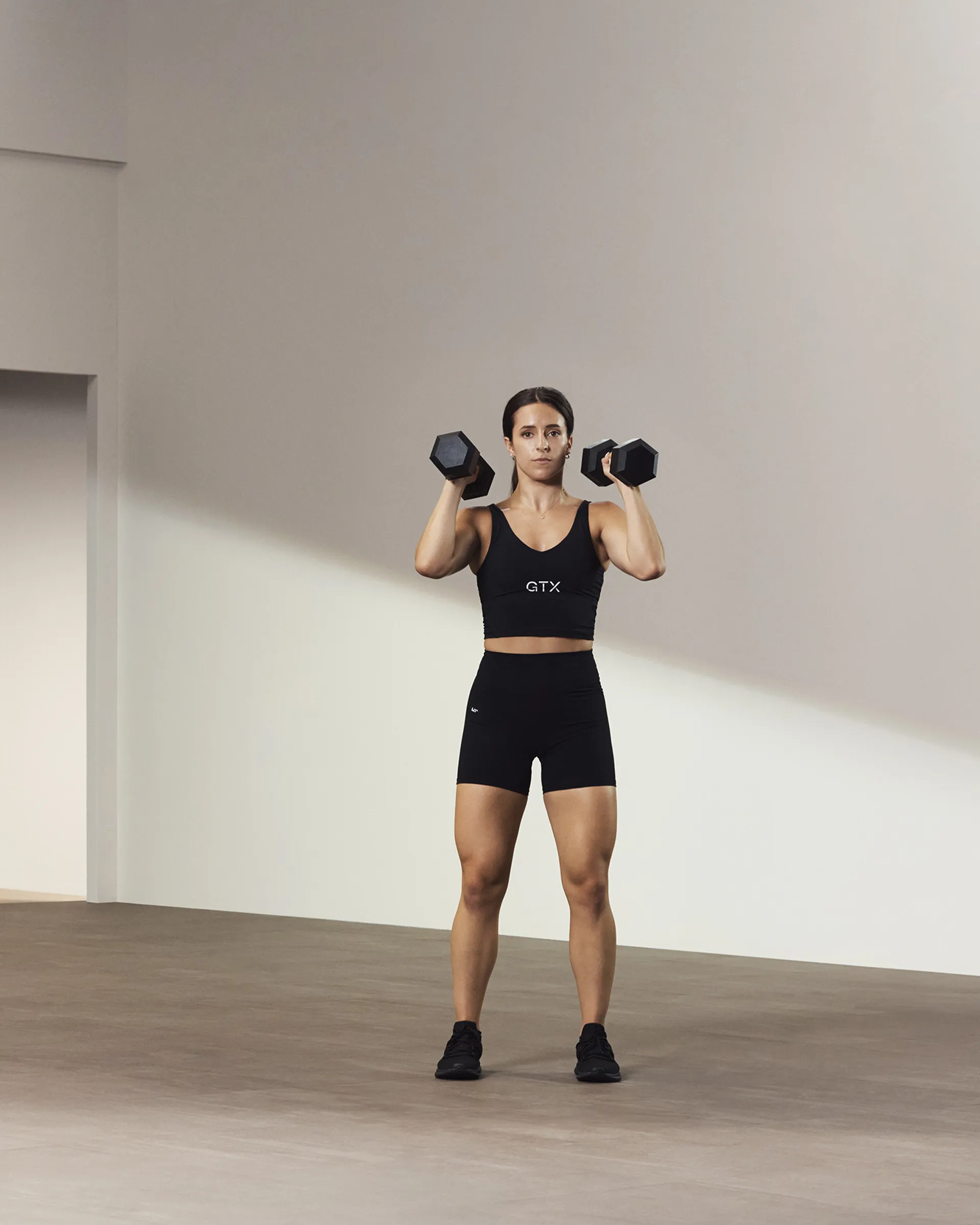 A Life Time member holding two dumbbells above their shoulders.